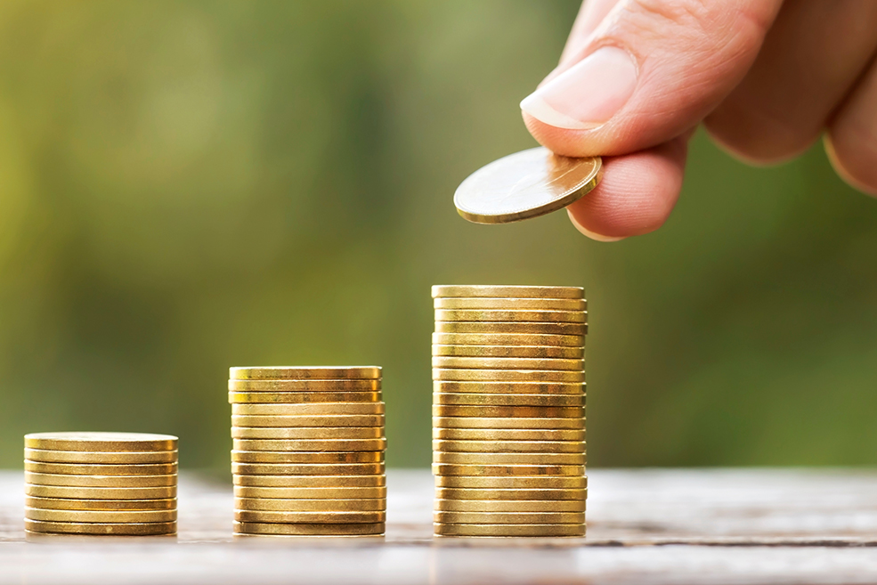 Growing gold money coins and hand, financial services concept, banner Three stacks of gold coins of increasing size with a hand adding a coin to the third stack.
