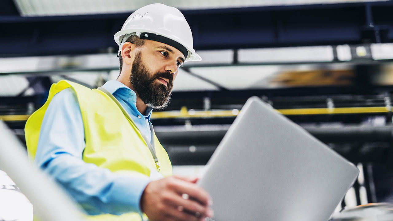 A portrait of an industrial man engineer with laptop in a factory, working. Male industrial engineer working in a factory using Minitab's structured problem-solving tools on his tablet.